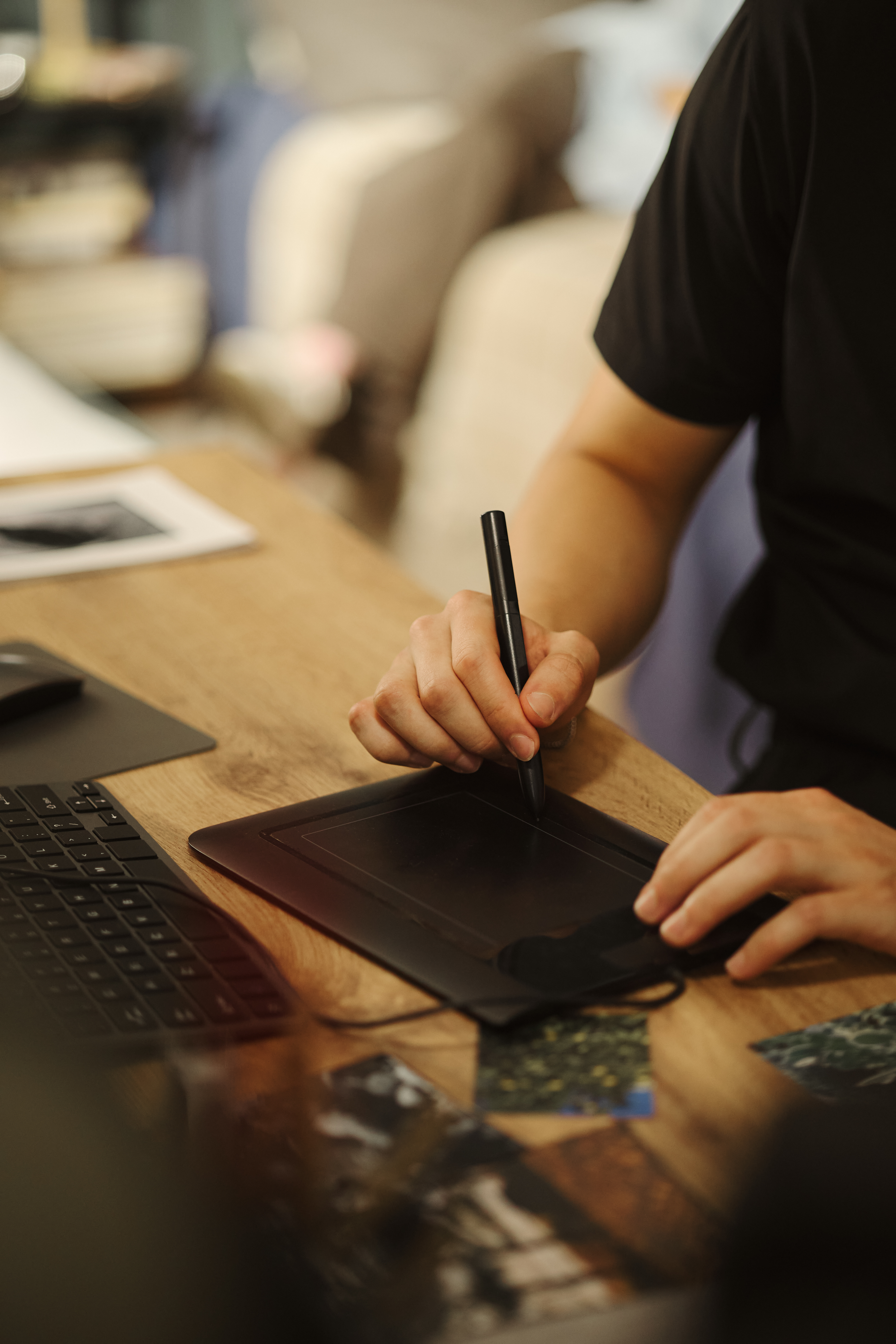 Young male designer drawing on digital graphic tablet with stylus at wooden desk. Image represents creative digital workflow, suitable for tech marketing, vertical